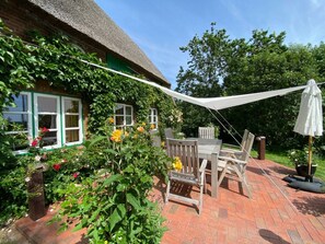Eine Pflasterterrasse mit Tisch und Stühlen, umgeben von einem Garten mit verschiedenen Pflanzen und Blumen.