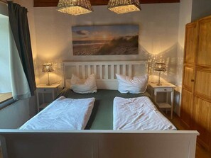 Ein Zimmer mit zwei Betten, einem weißen Kopfteil, einem Strandbild und zwei Nachttischlampen.
