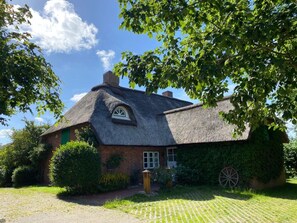A traditional thatched-roof house with a brick foundation, surrounded by lush greenery and a clear sky. - Holiday Home With 2 Bedrooms (St. Peter-Ording)