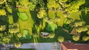 Vista aérea de un campo de golf con varios hoyos, rodeado de árboles y un edificio.