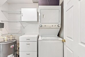 A laundry room with a front-loading washer and dryer, a small cabinet, and a water heater.