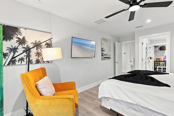 A bedroom with a bed, a chair, a ceiling fan, and wall art.