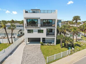 A modern two-story residential building with a flat roof, large windows, and a balcony.