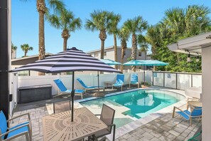 A swimming pool with lounge chairs and umbrellas, surrounded by palm trees.