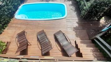 A wooden deck with a swimming pool and three lounge chairs.