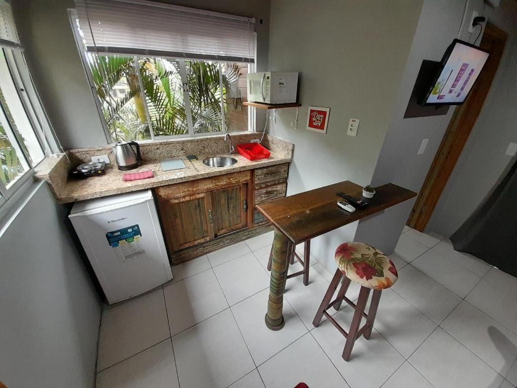 Una cocina compacta con refrigerador, pileta y una mesa de madera con un taburete.