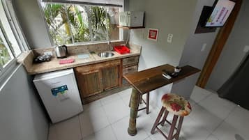 Una cocina compacta con refrigerador, pileta y una mesa de madera con un taburete.