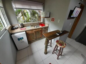 A compact kitchen with a refrigerator, sink, and wooden table with a stool.