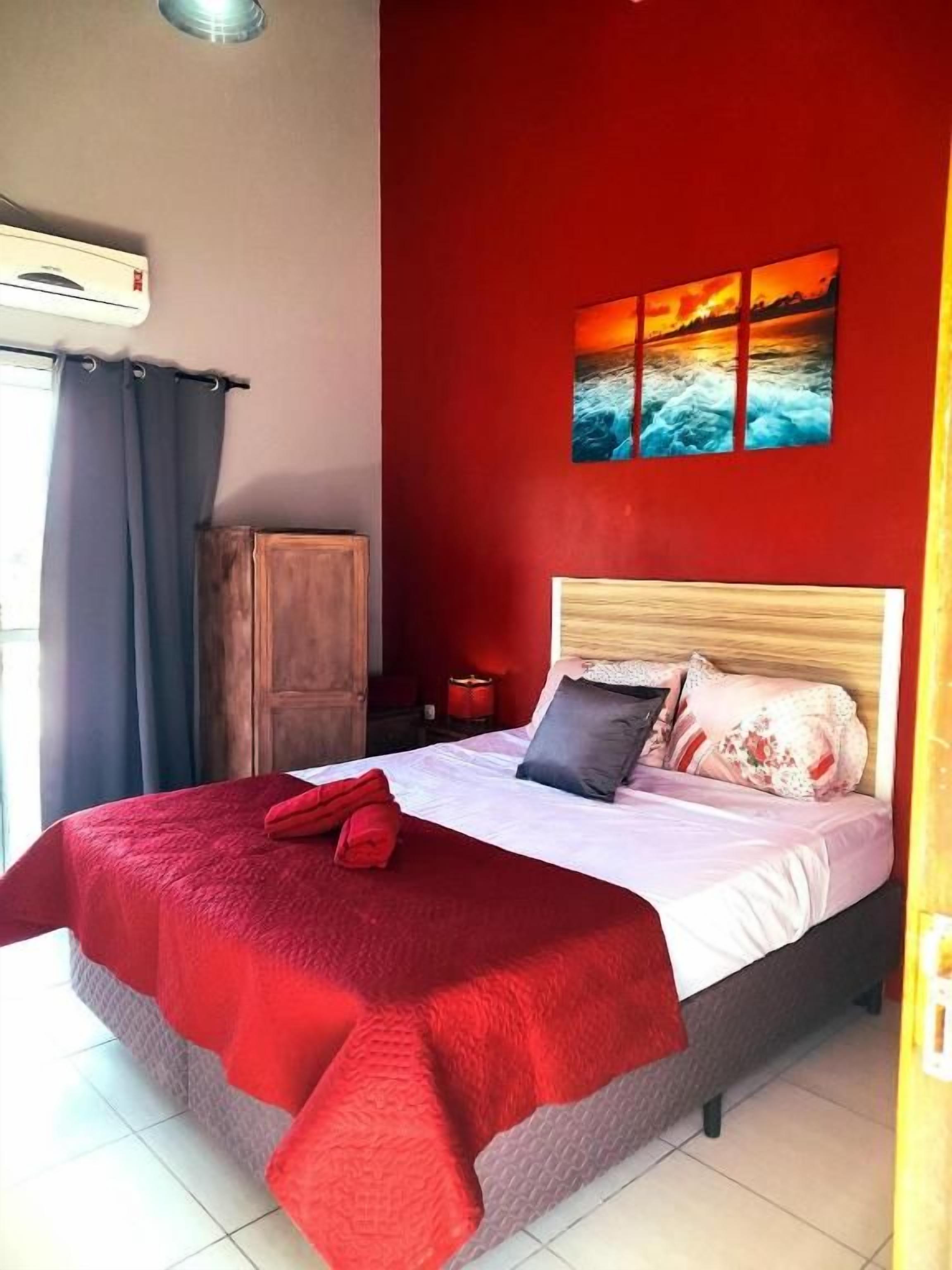 Un lit avec une couverture rouge, une tête de lit en bois et un tableau représentant un coucher de soleil accroché au mur.