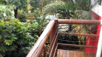 A wooden deck with a railing, surrounded by lush greenery and palm trees.