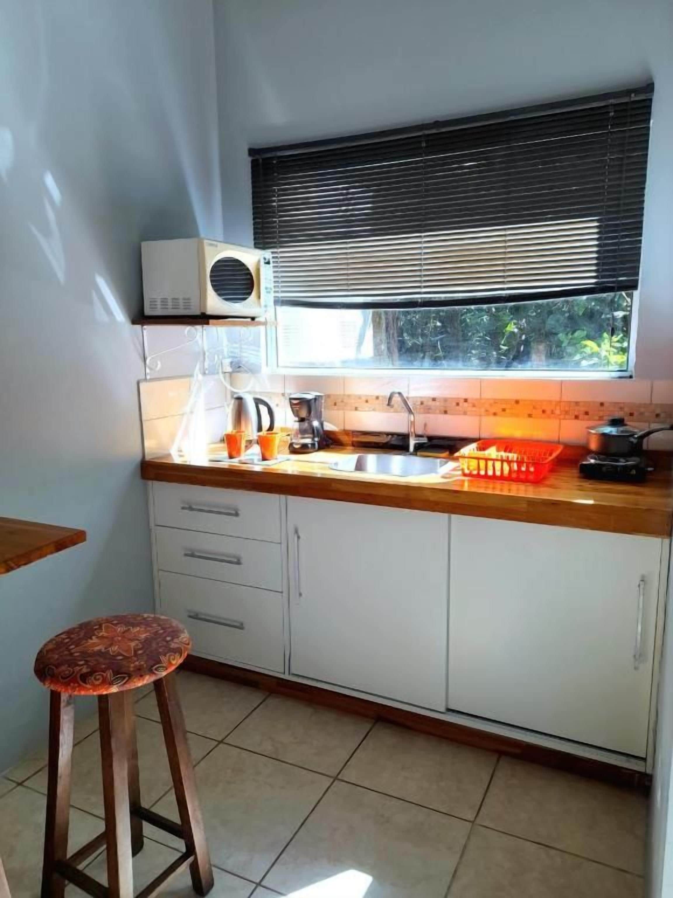Cozinha compacta com janela, forno embutido e um banquinho.