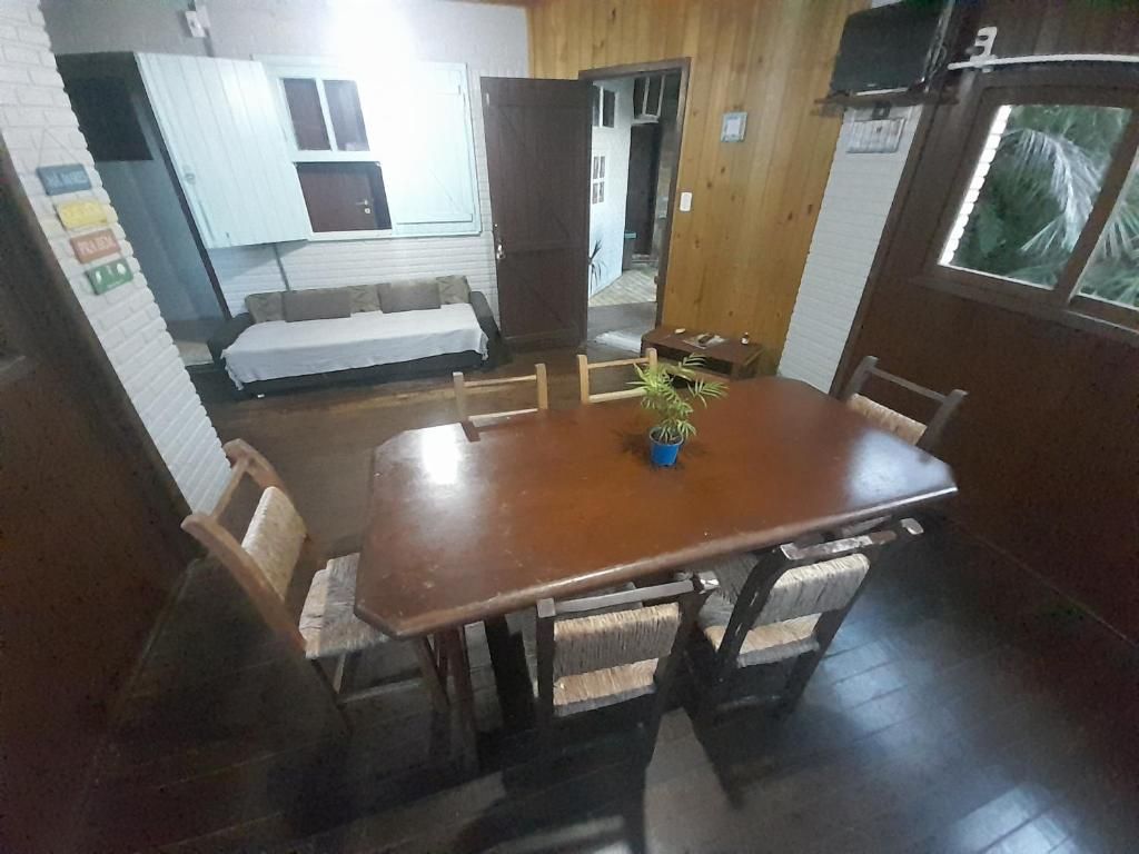 Un comedor con una mesa y sillas de madera, una planta en maceta y vistas a una habitación con cama y ventana.