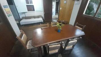Un comedor con una mesa y sillas de madera, una planta en maceta y vistas a una habitación con cama y ventana.
