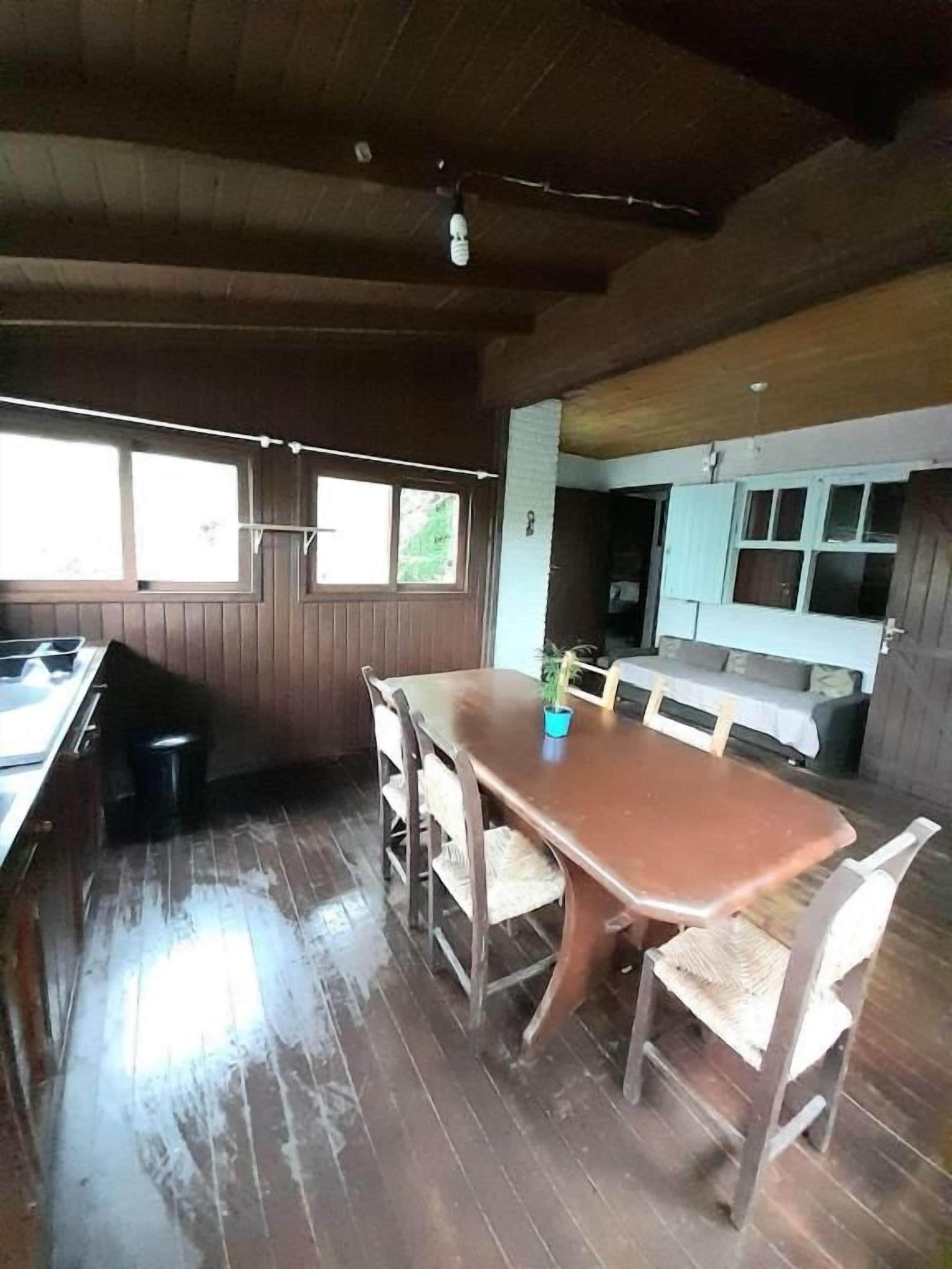 A wooden dining table with chairs, a kitchen area with cabinets, and a window with blinds.