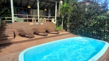 Une piscine avec une terrasse en bois, des chaises longues et un espace salon couvert agrémenté de parasols.