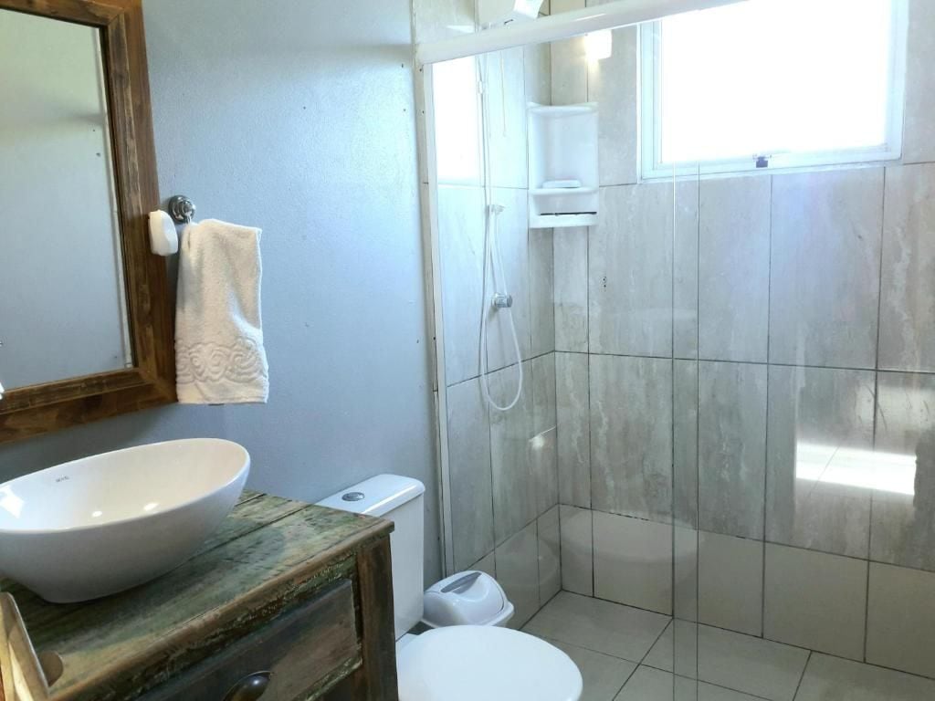 Un baño con un lavamanos grande de color blanco, un inodoro, zona de ducha y una ventana que proporciona luz natural.