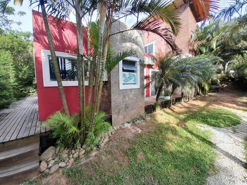 Un edificio rojo con una ventana y una puerta, rodeado de palmeras y una terraza de madera.