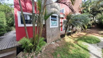 Un edificio rojo con una ventana y una puerta, rodeado de palmeras y una terraza de madera.