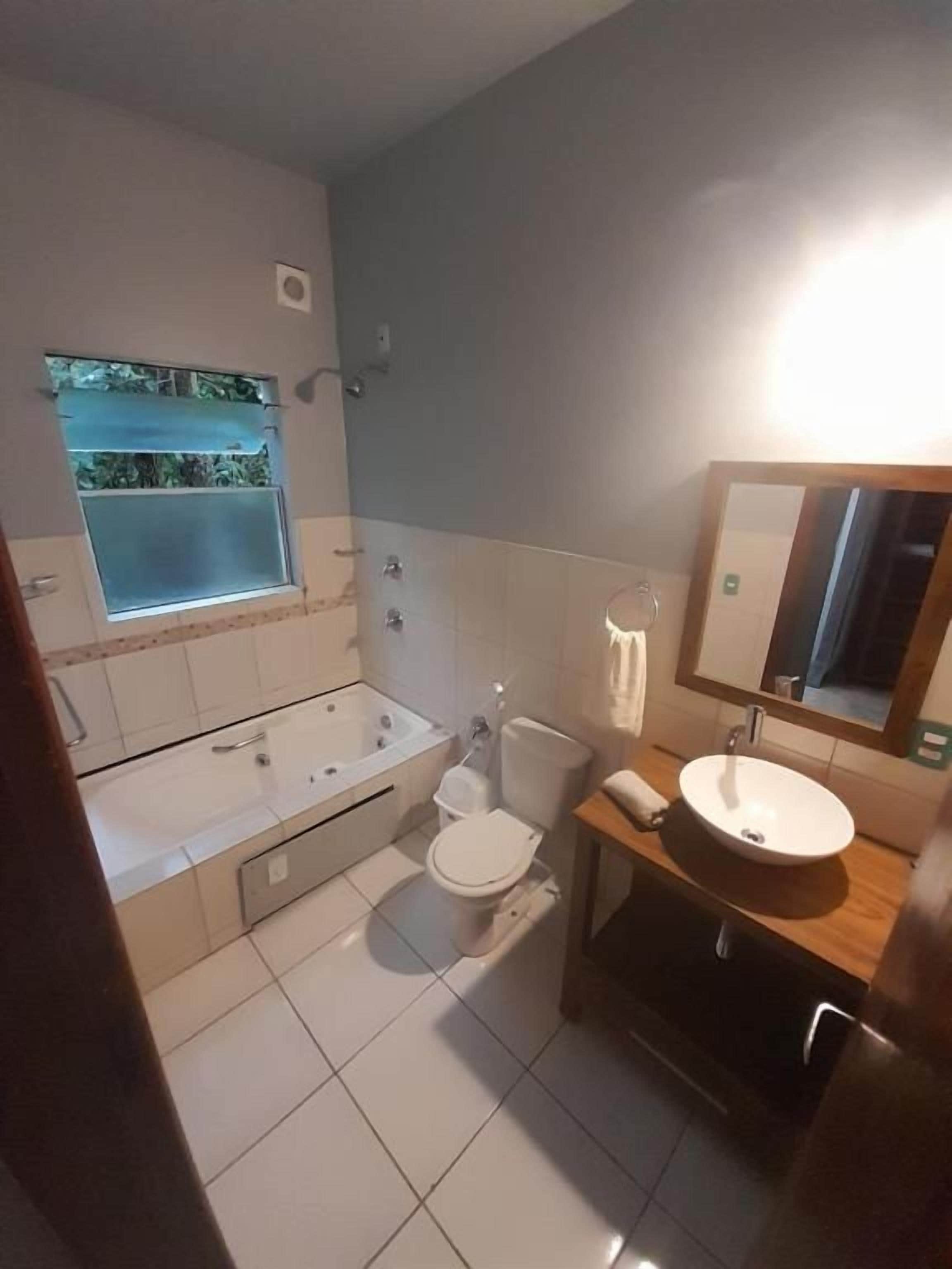 Et badeværelse med badekar, toilet, håndvask og et vindue med udsigt.