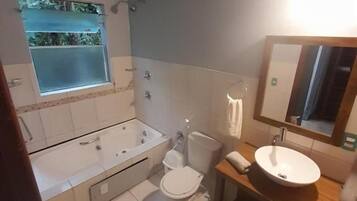 Et badeværelse med badekar, toilet, håndvask og et vindue med udsigt.