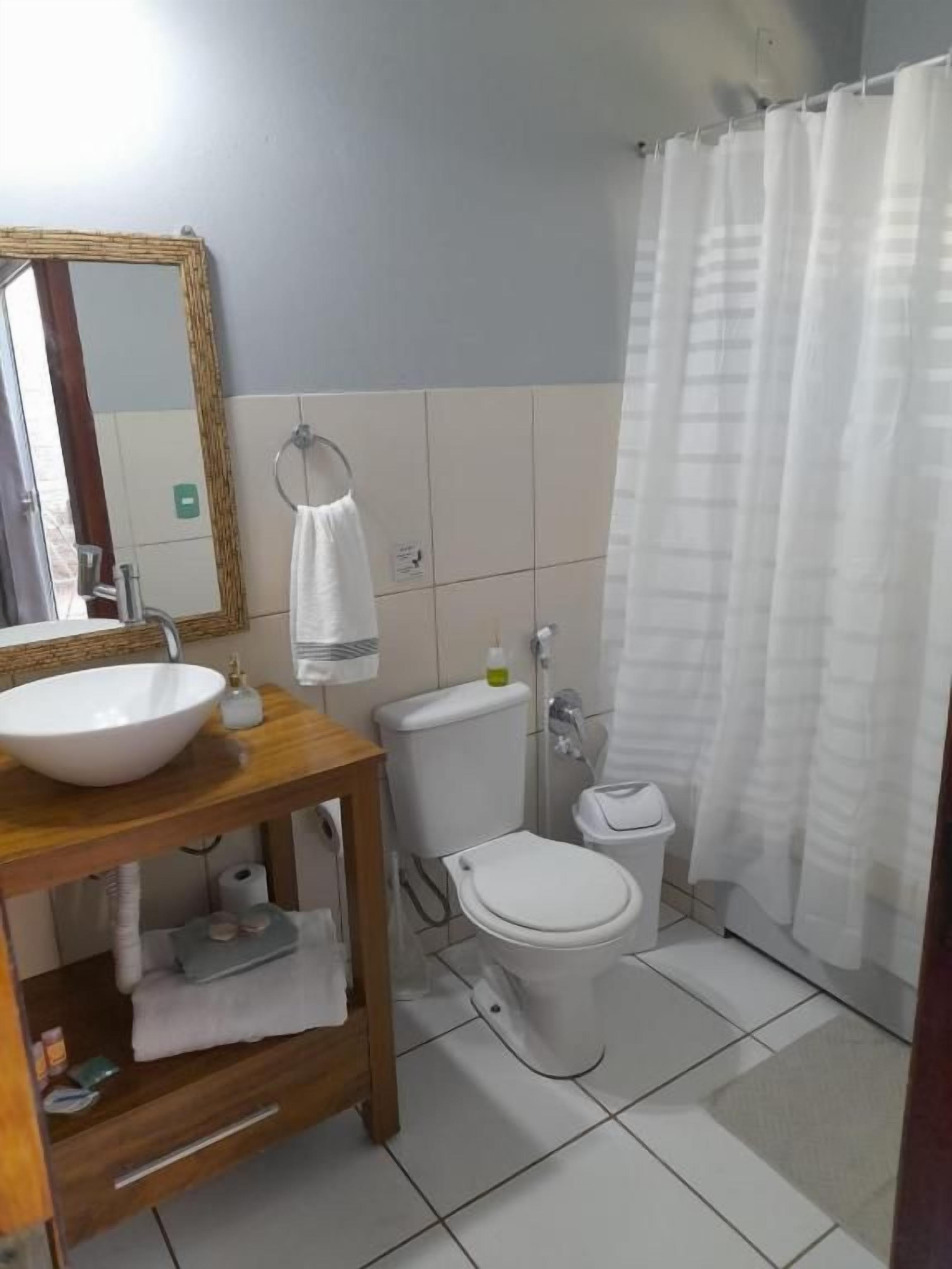 Un baño con tocador de madera, lavamanos blanco, inodoro y cortina de ducha.
