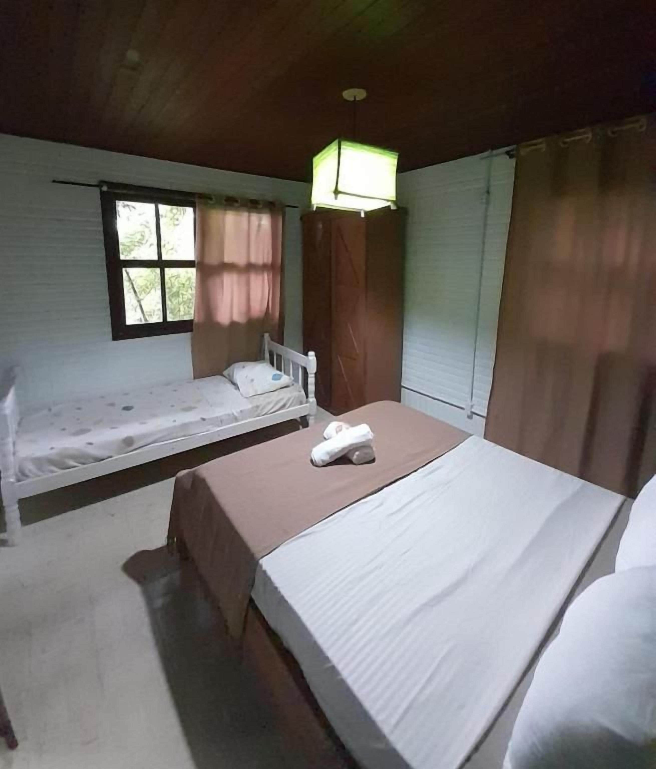 Una habitación con dos camas, una ventana con cortinas, una lámpara colgante y techo de madera.