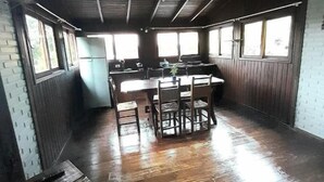 A spacious room with a wooden floor, a central dining table, and a kitchen area with a refrigerator. - Pousada Baia Rosa (Imbituba)