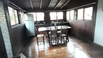 Une pièce spacieuse dotée d’un plancher en bois, d’une grande table à manger et d’un coin cuisine avec un réfrigérateur.