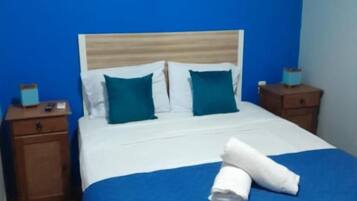 Habitación de hotel con cama, paredes azules, un cuadro y una mesita de noche con lámpara.