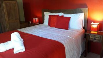 Una cama con una colcha roja y blanca, dos almohadas rojas y una toalla blanca sobre la cama. Hay dos lámparas de noche a cada lado de la cama.