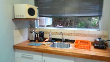 Una cocina con ventana, microondas, cafetera, pileta y escurreplatos.
