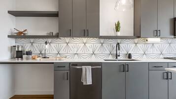 A modern kitchen with grey cabinets, a black faucet, and a geometric backsplash.