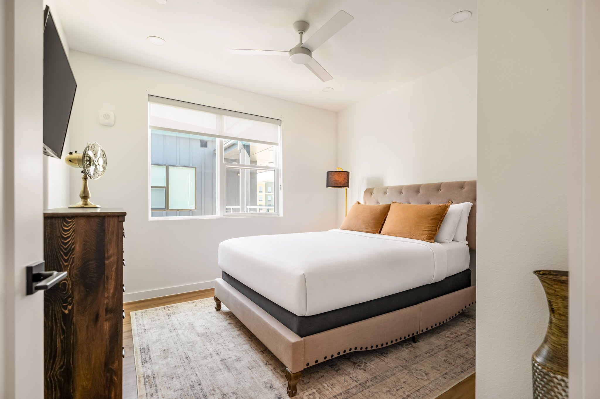 Een slaapkamer met een bed, een plafondventilator, een raam en een houten dressoir.