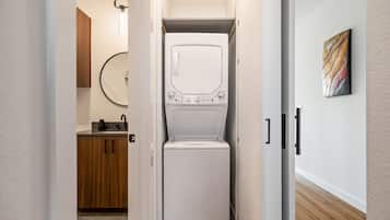 A laundry room with a front-loading washer and dryer, wooden cabinets, a round mirror, and a modern light fixture.