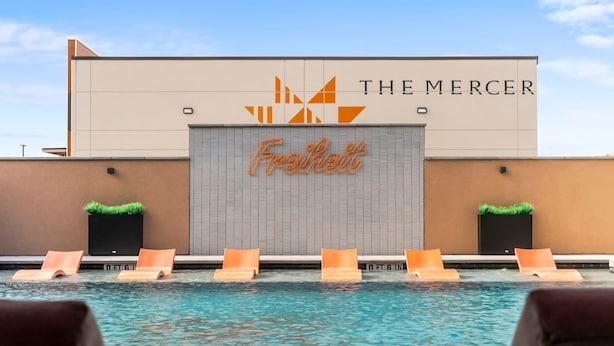 Un espace piscine avec des chaises longues et un bâtiment portant les enseignes « The Mercer » et « Freshert ».