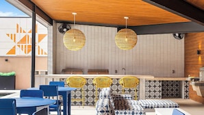 Un espace extérieur moderne, aménagé avec des tables et des chaises bleues, des chaises en osier jaune et des coussins à motifs.