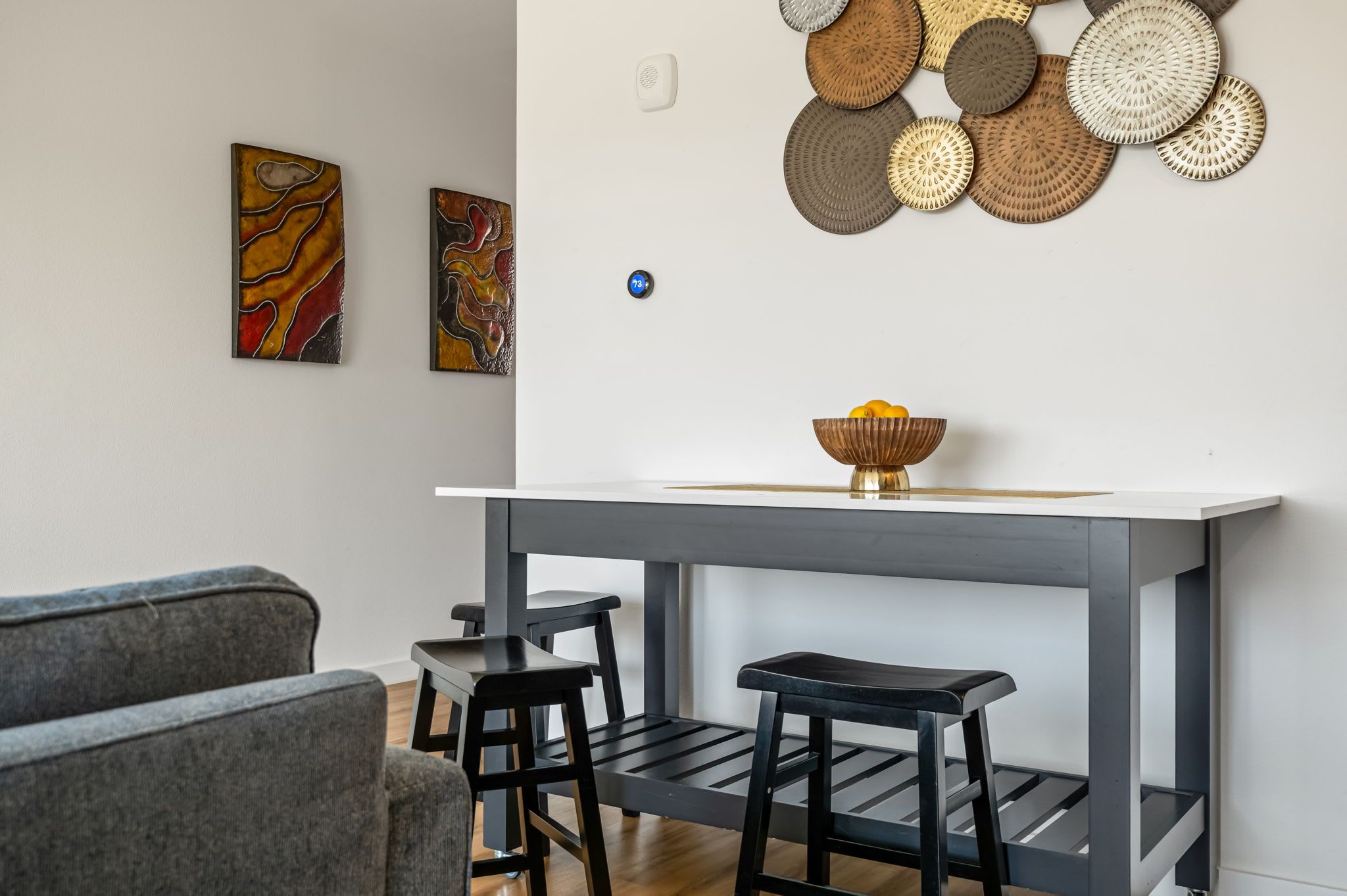 A modern living room with a grey console table, two black stools, and a grey sofa.