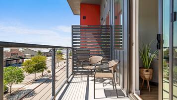 A balcony with a metal railing, two wicker chairs, a small table, and a potted plant.