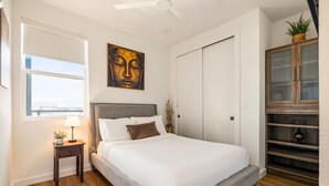 Une chambre à coucher comprenant un lit, une table de chevet, une lampe, un tableau, une armoire et une vue sur la ville.