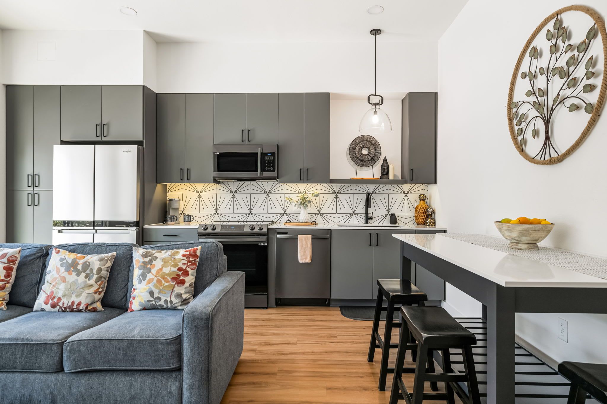 A modern kitchen with grey cabinets, a microwave, and a central island with stools.