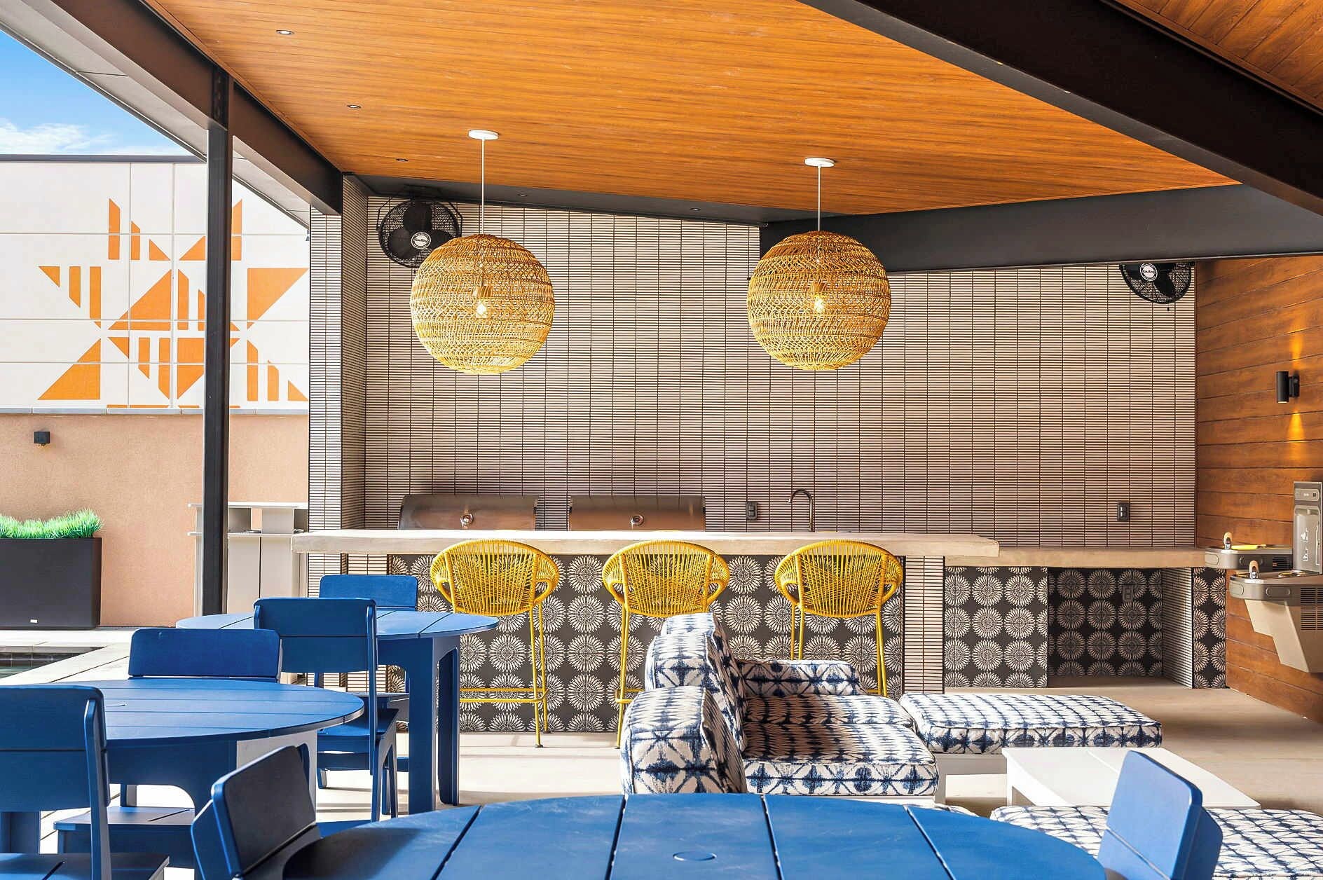 Een moderne buitenruimte met blauwe tafels en stoelen, gele geweven stoelen en gestreepte kussens.