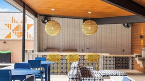 Un espace extérieur moderne, aménagé avec des tables et des chaises bleues, des chaises en osier jaune et des coussins à motifs.