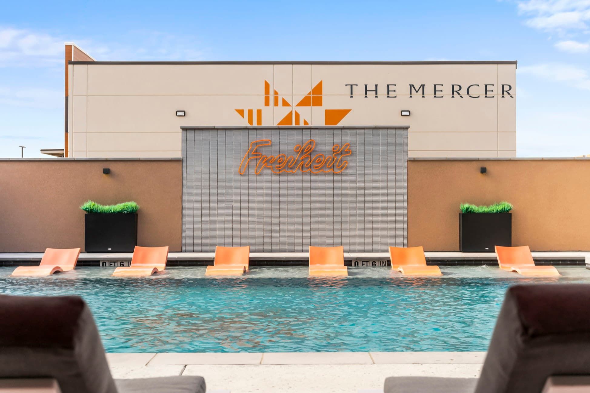Een zwembadgedeelte met ligbedden en een gebouw met de aanduiding 'The Mercer' en 'Freshert'.