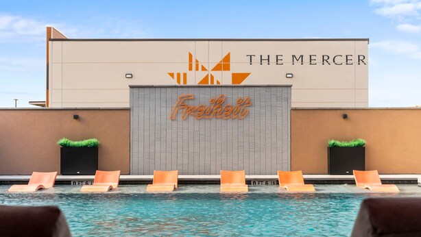 Un espace piscine avec des chaises longues et un bâtiment portant les enseignes « The Mercer » et « Freshert ».