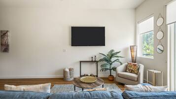 A modern living room with a flat-screen TV mounted on the wall, a round coffee table with decorative items, a sofa, and a potted plant.