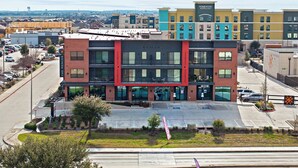 Un hôtel à plusieurs étages, doté d’une architecture moderne, qui se distingue par sa façade rouge et noire, ses nombreux balcons et un parking situé à l’avant.