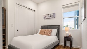 Une chambre à coucher avec un lit, une table de chevet avec une lampe, une fenêtre donnant sur un paysage et une porte.