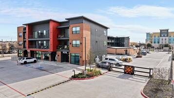 A multi-story hotel with a modern design, featuring a mix of brick and metal exterior, multiple balconies, and a parking lot with a few cars.