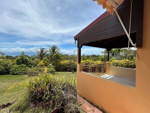 A house with a covered porch overlooking a lush garden and distant mountains. - A Getaway in Gosier: Spacious, Quiet Villa with Ocean and Mountain Views (Le Gosier)