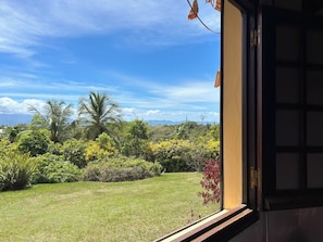 A view from a window overlooking a grassy area with various trees and shrubs, and a clear blue sky. - A Getaway in Gosier: Spacious, Quiet Villa with Ocean and Mountain Views (Le Gosier)